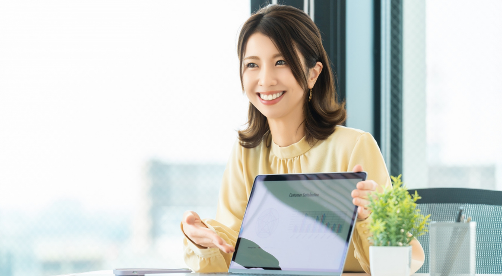 オフィスで女性が笑顔でノートパソコンのグラフ画面を見せながらプレゼンをしている画像で、【脳・全身(中枢神経・姿勢維持筋周辺)】を示し、首肩こりなどの不調が解消されたことで集中力がアップし、明るい表情で仕事のパフォーマンスが高まっている様子。